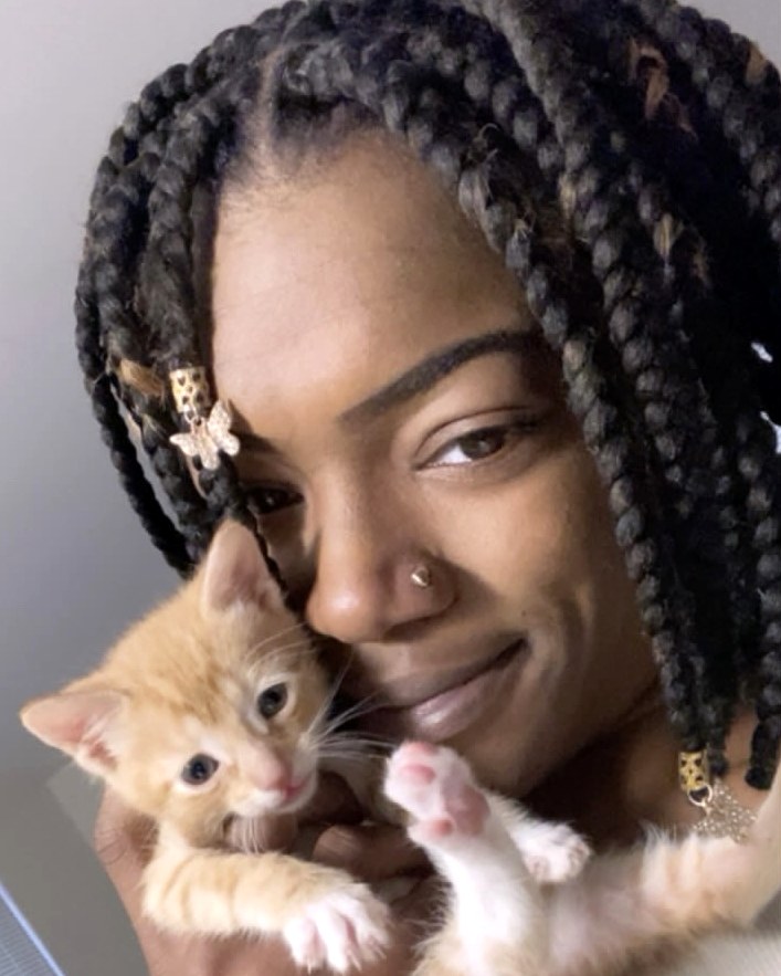 Kayy, founder of House Plenty Paws, smiling while gently holding a ginger kitten